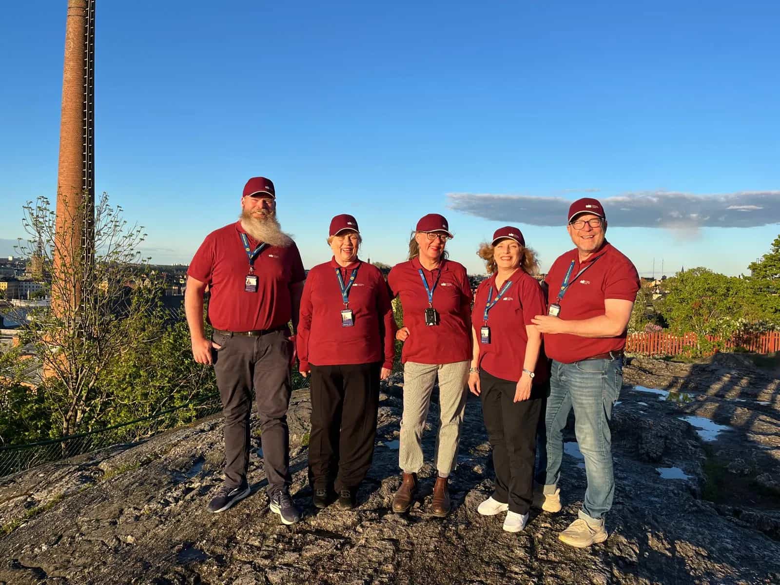 Five private guides in Stockholm in red uniforms on a cliff with a city view in the background