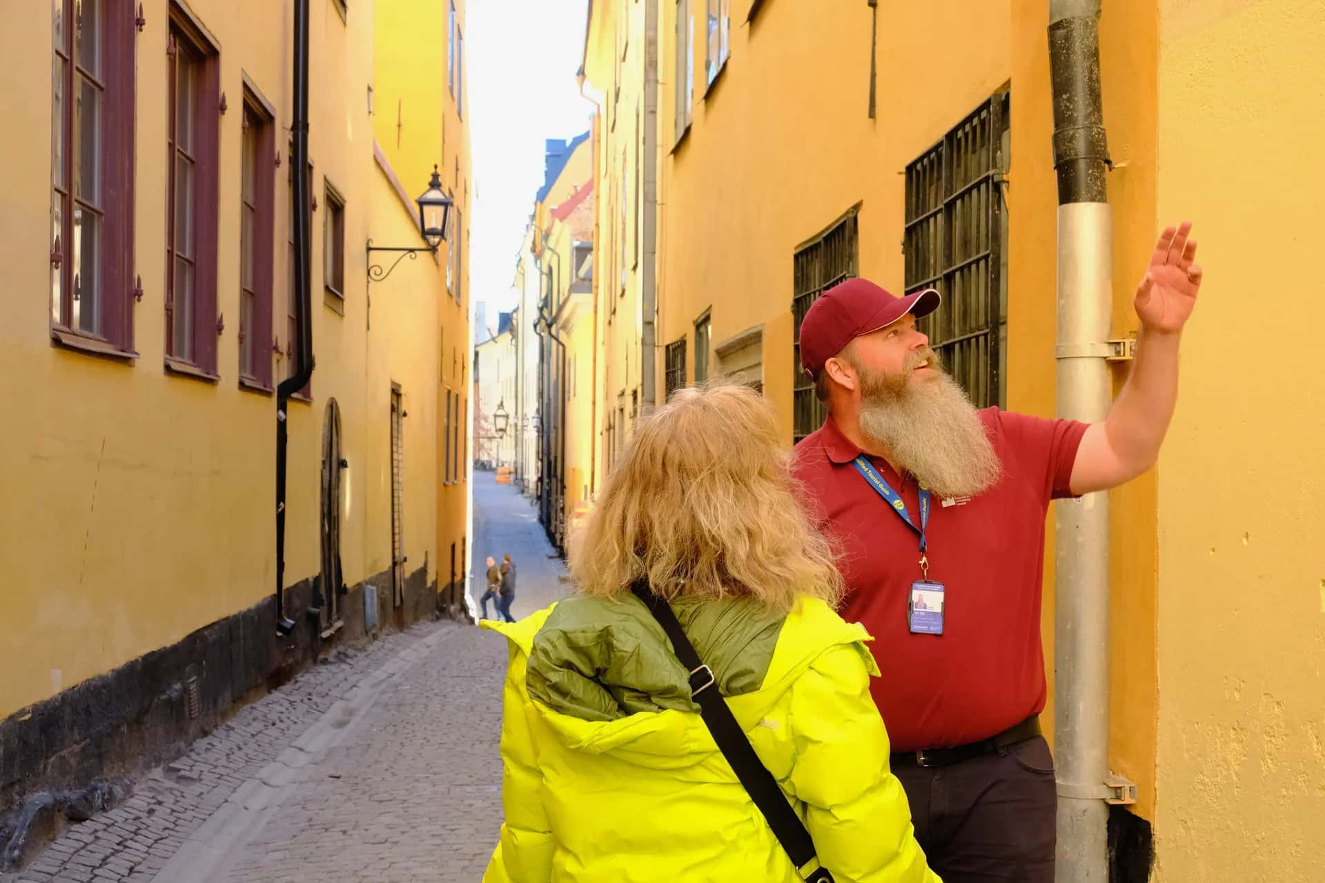 En man från Stockholms auktoriserade guider pekar för en kvinna i en smal gränd med gula hus